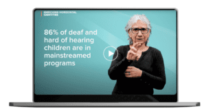 A Caucasian woman with grey hair and glasses wearing a black sweater signs into camera. Next to her is a text graphic on a lap top that reads: "86% of deaf and hard of hearing children are in mainstreamed programs."